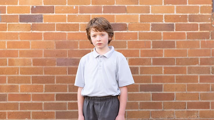 Boy standing in school unform against a brick wall