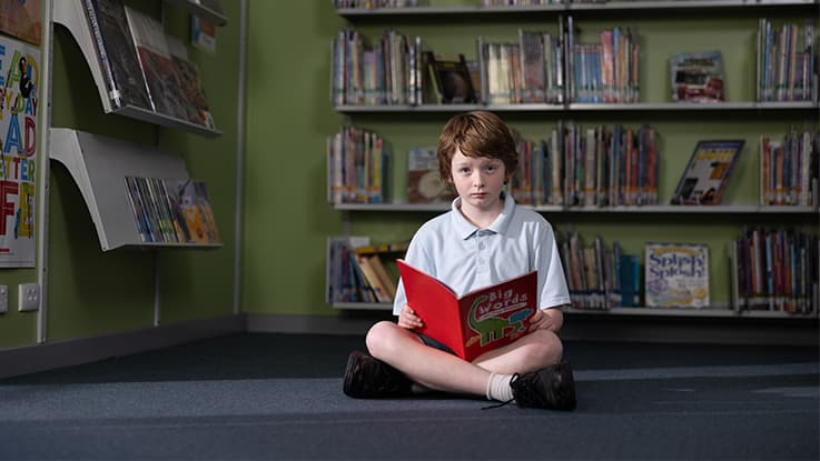 Boy sitting on library floor reading a book