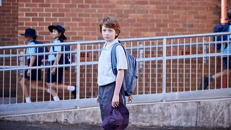 Boy standing in playground with school kids behind