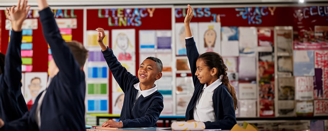 students in a classroom holding up their hands