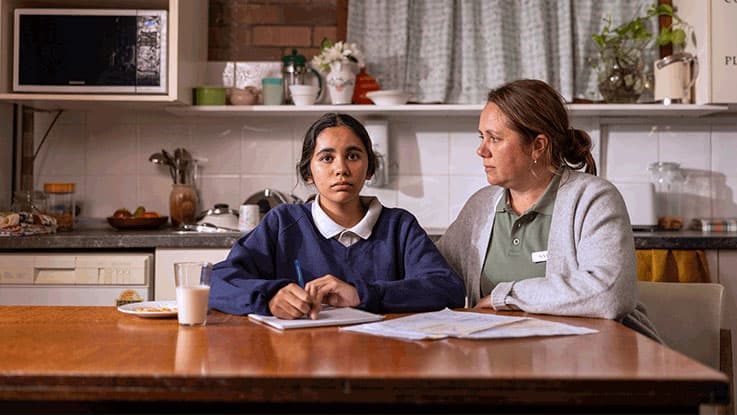 Teenage girl sitting with her mum in their home kitchen