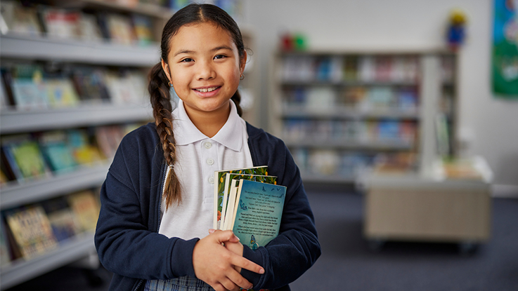 a school girl holding books in the library smiling 