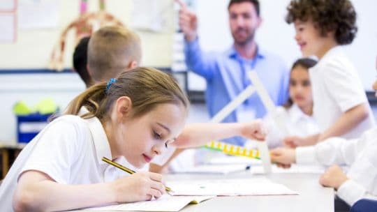 A girl seating on desk in class and writing in notebook