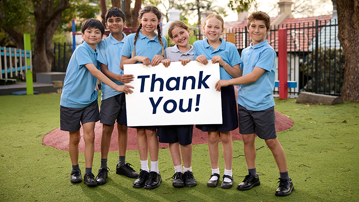 students holding a thank you sign smiling and standing in a playground