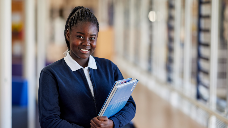 student holding books smiling in library