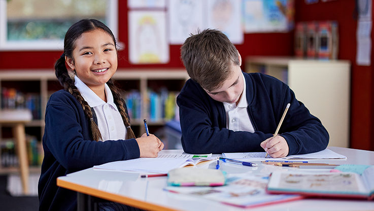 a school girl is smiling and drawing with a school boy in a classroom