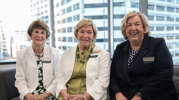 three ladies sitting down smiling together by a window