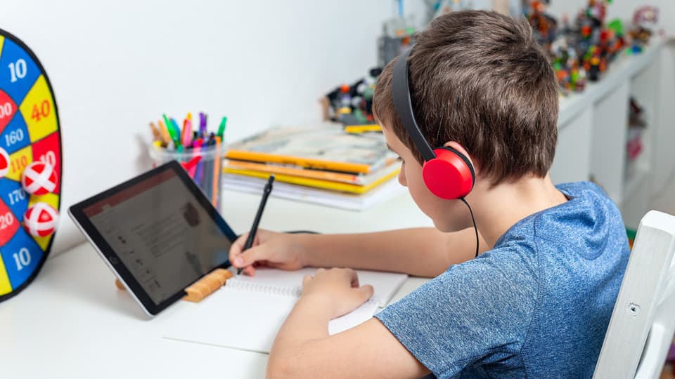 child studying online at desk with tablet and headphones