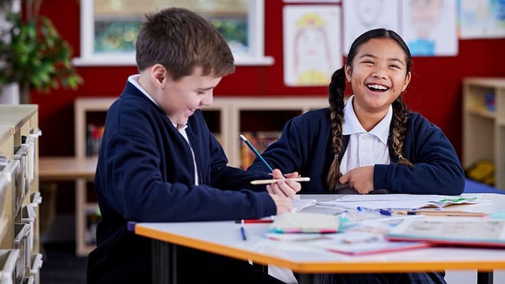 Two school children laughing while doing an activity at their desks