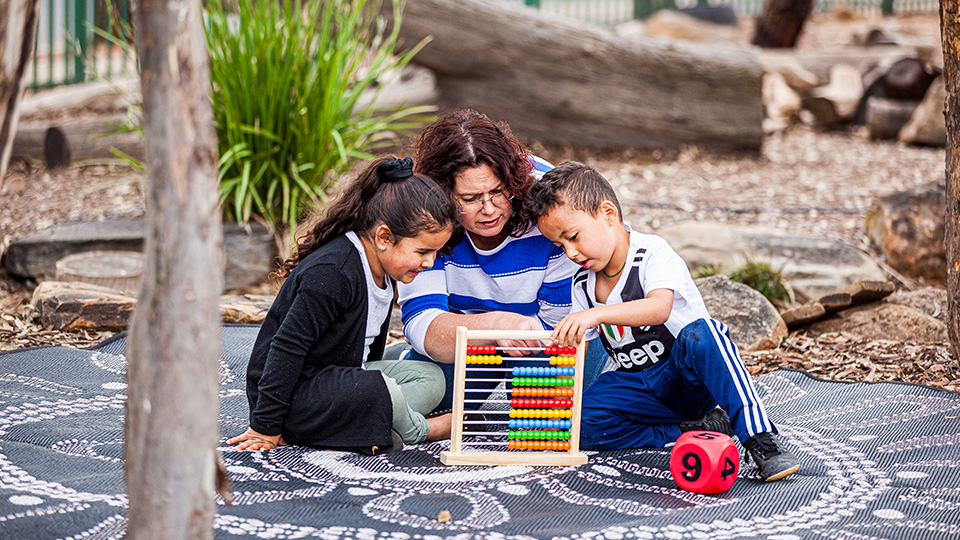 three people sitting outdoors with an abacus and a large red die