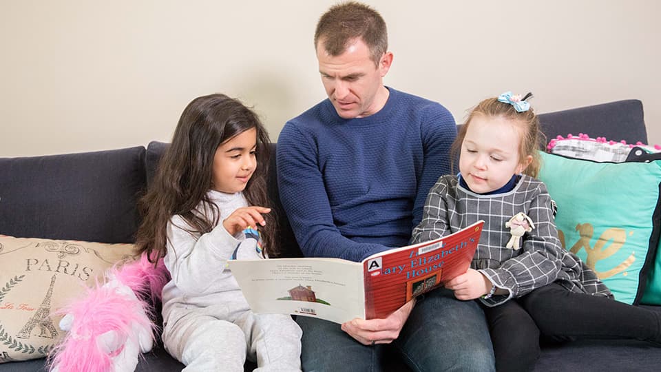 a person reading a book titled 'Mary Elizabeth's House' to two children on a couch