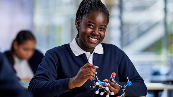 A smiling young female school student holding a molecular model in a classroom