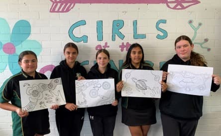 five young women holding up indigenous illustrations or artworks